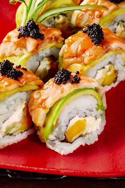 Closeup of uramaki rolls with cream cheese, mango, avocado, shrimp and black tobiko on red plate — Stockfoto