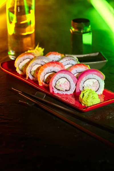 Assorted sushi rolls on plate and drink served on bar counter lighted by LED strip — Stockfoto