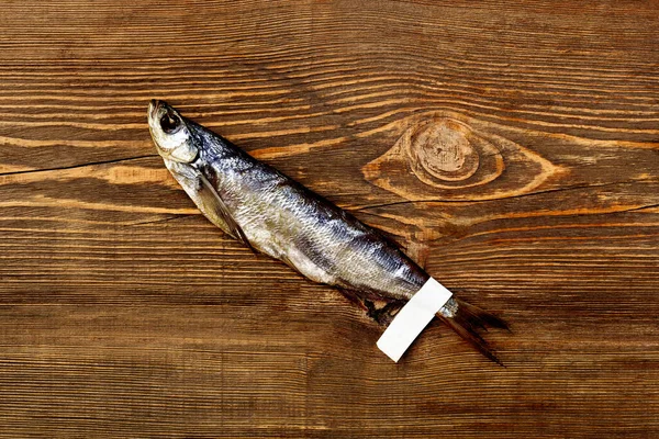 Соленая балтийская сельдь с бумажной этикеткой на хвосте на деревянном столе — стоковое фото