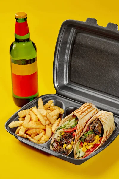 Vegan burrito in takeaway container with fries and bottle of drink on yellow background — Fotografia de Stock