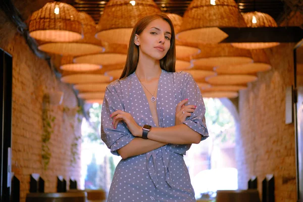 Menina loira em vestido azul longo, relógio, anel está posando de pé sob um enorme lustres em um café da cidade. Imagem de close-up. — Fotografia de Stock