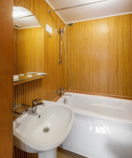 Interior of small bathroom in hotel room with wooden walls, white wash basin and bathtub — Stockfoto