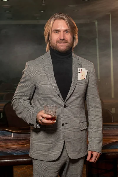 Χαμογελαστή άνθρωπος με δύο άσους στην τσέπη σακάκι και ένα ποτήρι ποτό στο καζίνο smokey — Φωτογραφία Αρχείου