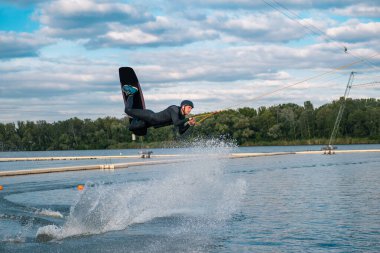 Kendinden emin erkek wakeboardcu yaz günü göl yüzeyinde atlıyor.
