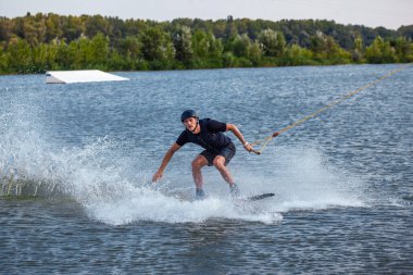 Wakeboard 'da dengede duran bir adam kabloyla çekilip tahtaya tutunmaya çalışıyor.