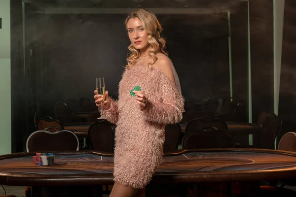Magabiztos női pókerjátékos egy pohár pezsgővel és zsetonnal a játékasztal mellett — Stock Fotó