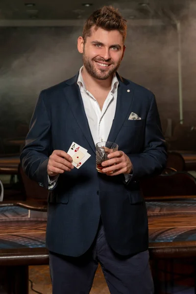 Успішний гравець в покер стоїть біля ігрового столу з парою асів і келихом напою — стокове фото