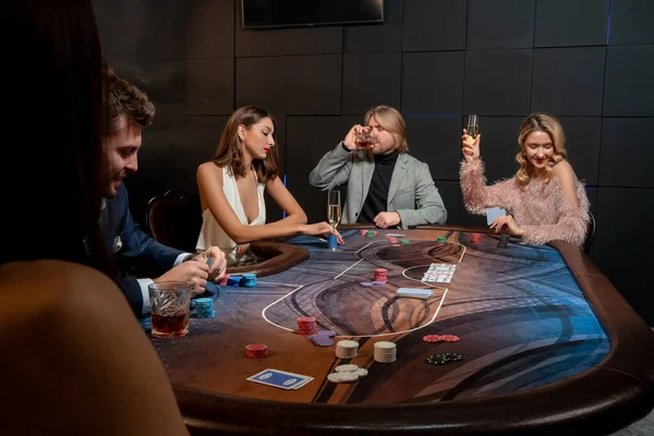 Hazardní hry muži a ženy hrají poker u herního stolu a pití alkoholu — Stock fotografie