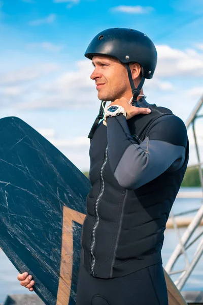 Konzentrierter Wakeboarder in voller Montur, der auf einem Steg mit Brett steht und gespannt wegschaut — Stockfoto