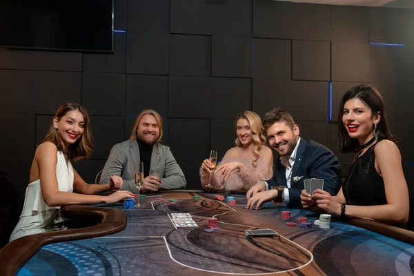 Adultos alegres sentados en la mesa de juego con cartas, fichas de apuestas y bebidas alcohólicas —  Fotos de Stock