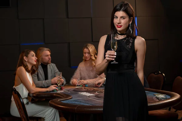 Usmívající se mladá brunetka se sklenkou šampaňského u pokerového stolu — Stock fotografie