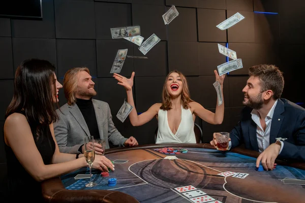 Nadšený dívka vyhrává poker, házet papírové peníze do vzduchu u herního stolu — Stock fotografie