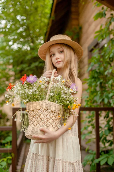 Preteen fille rêveuse avec panier de fleurs sauvages debout dans la cour de la maison rurale — Photo