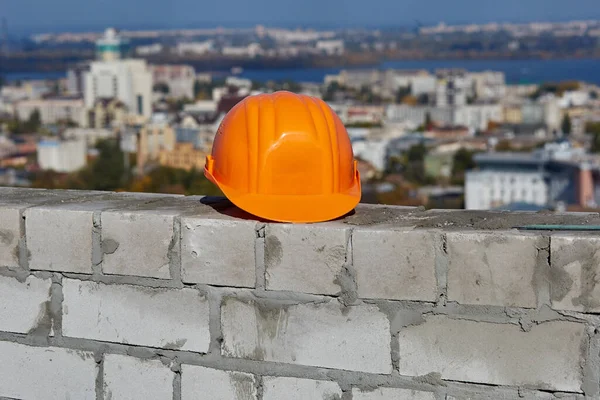 Casque de sécurité orange est sur un mur de briques. Toit du bâtiment moderne en construction. Paysage urbain panoramique pittoresque, ciel bleu, journée ensoleillée — Photo