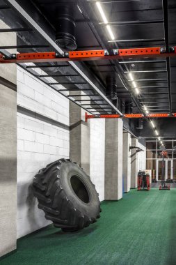 Geniş, boş bir spor salonunda duvara dayanmış kocaman siyah bir lastik. Fiziksel eğitim için özel modern ekipman. Spor, fitness, Crossfit