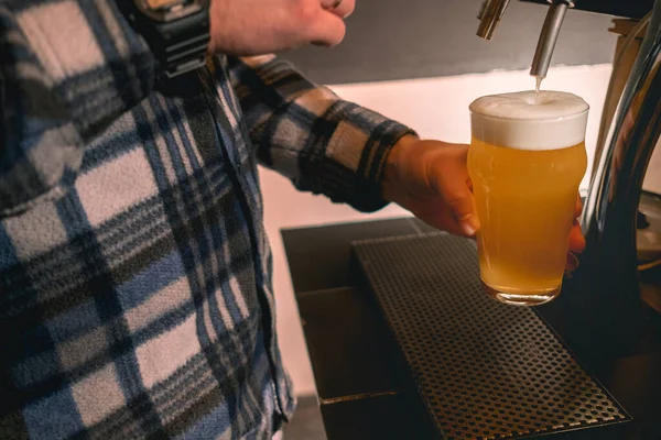 Bartender holding glass of beer under dispenser tap ready to serve to guest — Stock Photo, Image