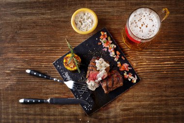 Mantar soslu ızgara biftek ve tahta masada bir kupa bira. Üst görünüm