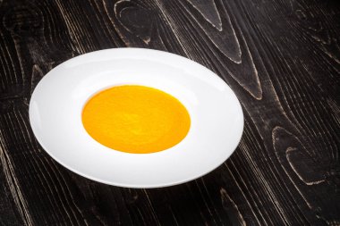 Siyah ahşap zemin üzerinde balkabağı çorbası olan bir kase.