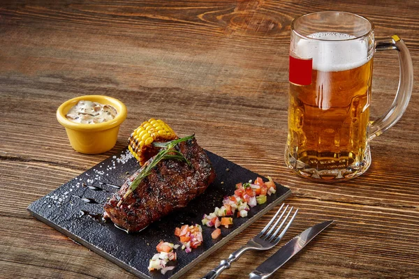 Grilled tenderloin Steak roastbeef and mushrooms sauce on black cutting board and glass of beer on wooden background — Stock Photo, Image