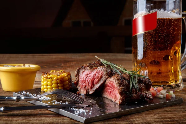 Gegrilltes Filet-Steak Roastbeef mit Pilzsoße auf schwarzem Schneidebrett und ein Glas Bier auf Holztisch — Stockfoto