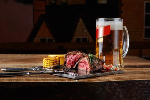 Grilled tenderloin Steak roastbeef and mushrooms sauce on black cutting board and glass of beer on wooden table — Stock Photo, Image