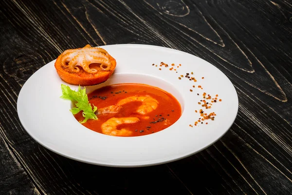 Миска томатного супу з креветками з невеликим восьминогом, запеченим на апельсиновому скибочці на чорному дерев'яному фоні, вид зверху — стокове фото