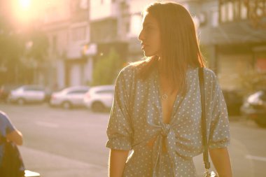 Uzun mavi elbiseli sarışın kız ve omzunda küçük siyah bir çanta şehirde tek başına yürüyor. Moda ve tarz. Yakın çekim..