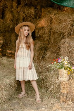 Samanlıkta duran renkli yabani çiçeklerle dolu sepetli genç kız.