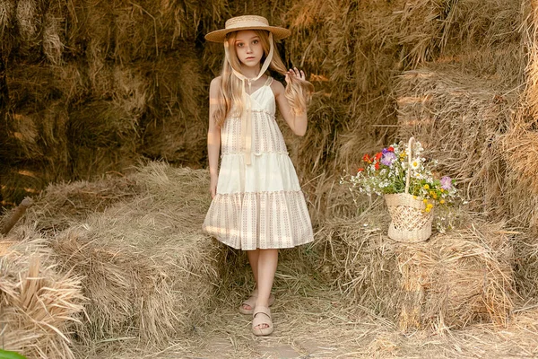 Блондинка-подросток позирует на сеновале с корзиной полевых цветов — стоковое фото