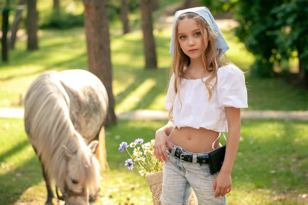 Dromerig meisje wandelen in groene zomer park op de achtergrond van grazende paard — Stockfoto