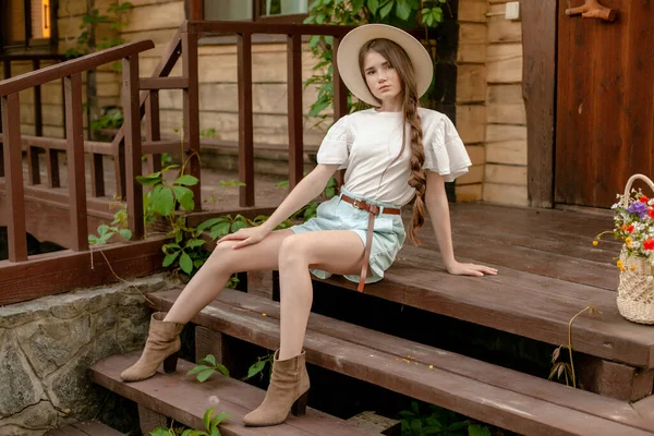 Brązowłosy nastolatek dziewczyna siedzi na drewnianych drzwiach wiejskiego domu w lecie — Zdjęcie stockowe