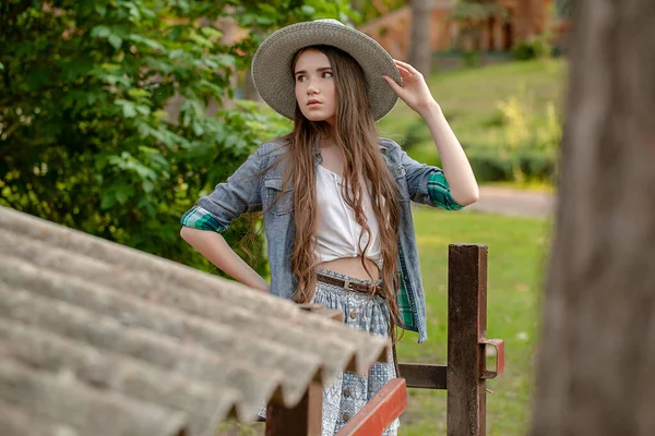Брюнетка-подросток в деревенской одежде стоит на зеленом заднем дворе загородного дома — стоковое фото