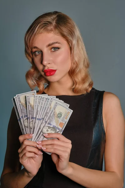 Blondynka w czarnej sukience trzymająca fankę studolarowych banknotów, pozująca na szarym tle. Hazard, poker, kasyno. Zbliżenie. — Zdjęcie stockowe