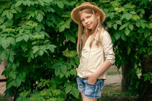 Glimlachend tussen een meisje dat bij de groene vlierbessenstruik staat in de zomertuin — Stockfoto
