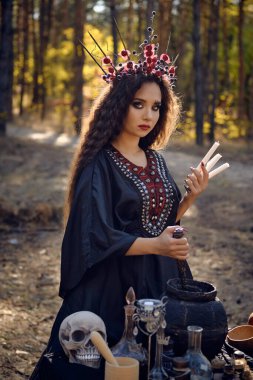 Siyah elbiseli, uzun elbiseli, uzun kıvırcık saçlı güzel bir cadı. Çam ormanında poz vermek. Büyü, büyü ve büyücülük. Yakın plan..