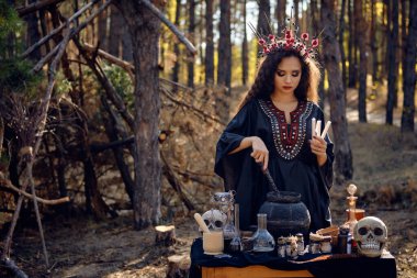 Siyah elbiseli, uzun elbiseli, uzun kıvırcık saçlı güzel bir cadı. Çam ormanında poz vermek. Büyü, büyü ve büyücülük. Yakın plan..