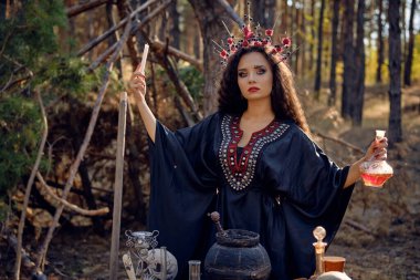 Siyah elbiseli, uzun elbiseli, uzun kıvırcık saçlı güzel bir cadı. Çam ormanında poz vermek. Büyü, büyü ve büyücülük. Yakın plan..