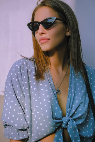 Menina loira em vestido azul longo, óculos de sol e uma pequena bolsa preta em seu ombro está andando sozinha na cidade. Moda e estilo. Imagem de close-up. — Fotografia de Stock