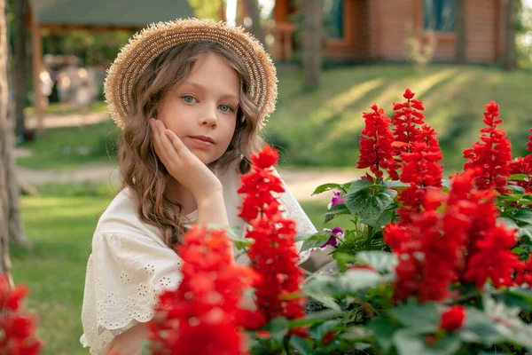 Мечтательная девочка-подросток позирует возле клумбы с цветущей красной сальвией в саду — стоковое фото