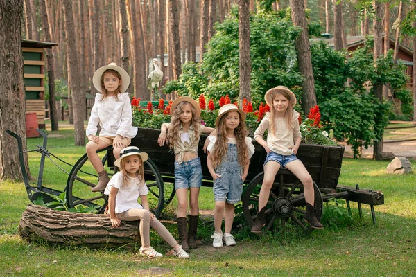 Groupe de filles préadolescentes amicales posant à côté d'un chariot en bois vintage conçu comme un lit de fleurs à l'extérieur — Photo