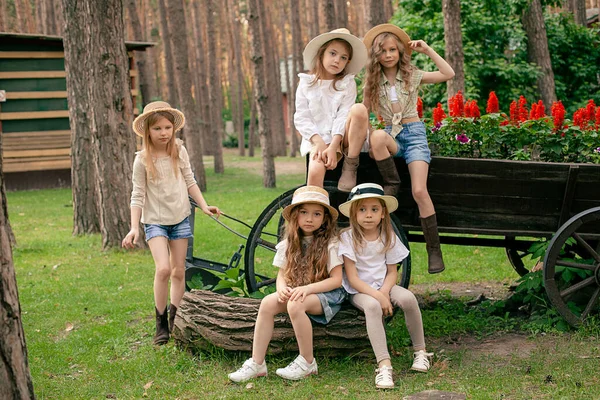 Group portrait of preteen girls near old wooden cart used as flower bed in park — стоковое фото