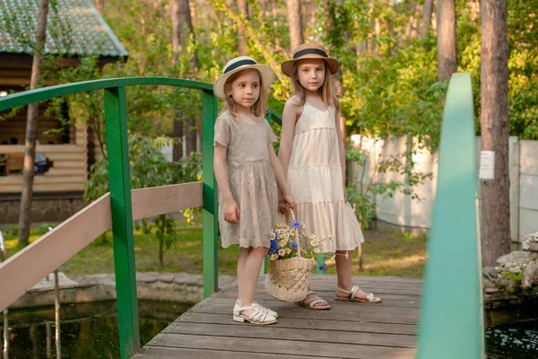 Tween zussen wandelen langs houten brug over kleine vijver in de tuin van het landhuis — Stockfoto