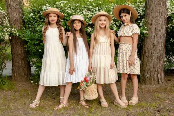 Весёлые девочки-подростки с корзиной цветов, позирующие возле цветущего кустарника в парке — стоковое фото