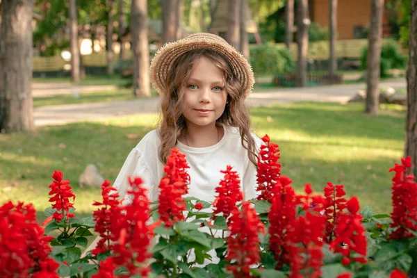 Souriant fille préadolescente posant à côté de fleurs rouges en fleurs à la propriété de campagne — Photo