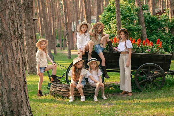 Веселые девочки-подростки позируют возле клумбы в виде деревянной тележки в летнем парке — стоковое фото