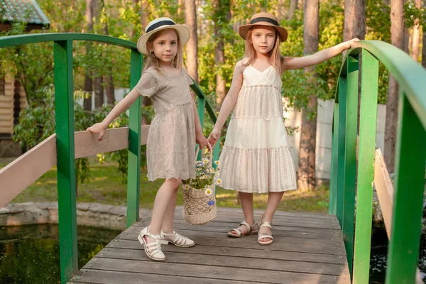 Preteen meisjes poseren op houten brug over kleine vijver in landgoed op zomerdag — Stockfoto