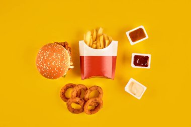 Fast food tepesi manzarası. Et burger, patates cipsi ve kama. Kompozisyonu kaldır. Patates kızartması, hamburger, mayonez ve sarı arka planda ketçap sosu..