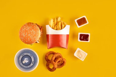 Fast food tepesi manzarası. Et burger, patates cipsi ve kama. Kompozisyonu kaldır. Patates kızartması, hamburger, mayonez ve sarı arka planda ketçap sosu..