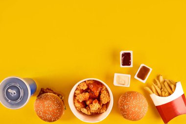 Fast food tepesi manzarası. Et burger, patates cipsi ve kama. Kompozisyonu kaldır. Patates kızartması, hamburger, mayonez ve sarı arka planda ketçap sosu..
