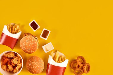 Fast food tepesi manzarası. Et burger, patates cipsi ve kama. Kompozisyonu kaldır. Patates kızartması, hamburger, mayonez ve sarı arka planda ketçap sosu..
